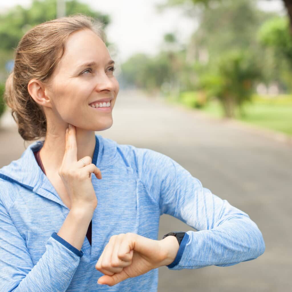 Closeup portrait of smiling young beautiful woman wearing sportswear and taking pulse outdoors